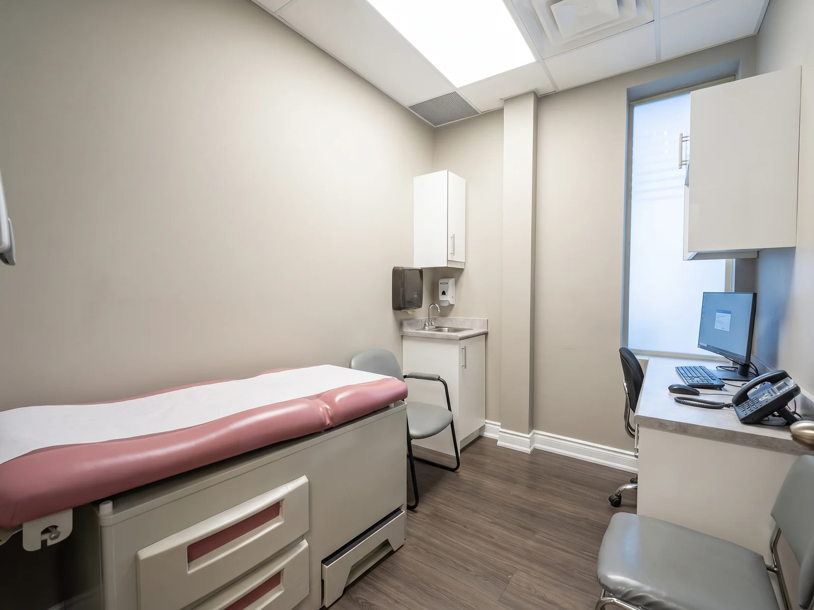 An examination room with an exam table, sink and cabinetry